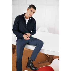 A navy half-zip jumper worn by a model, paired with navy trousers and black ankle boots, set in a modern interior.