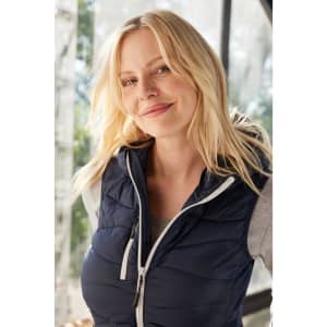 A navy blue ladies’ hybrid vest with a hood, featuring zip detailing and a branding logo.