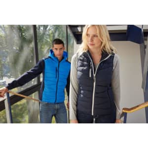 A navy ladies hybrid vest with a hood, featured alongside a blue jacket. The setting is bright with natural light.