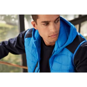 A men's hybrid vest in bright blue with a hood, featuring a quilted design and a navy base layer.