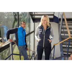 A blue and grey hybrid vest worn by a man and a woman. The scene features a modern staircase and windows.