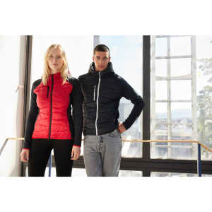 A red and black hybrid jacket worn by a woman and a man, featuring a logo and set against a bright indoor background.