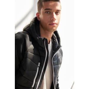 A men's hybrid jacket in black, featuring a zip closure and a hood, modelled by a young man.