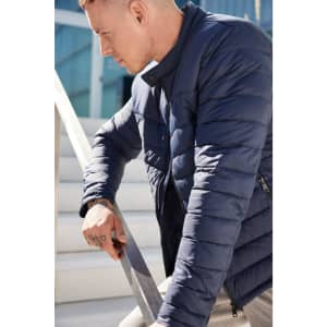 A navy padded jacket with a zip front and a high collar, styled on a man leaning against a railing.