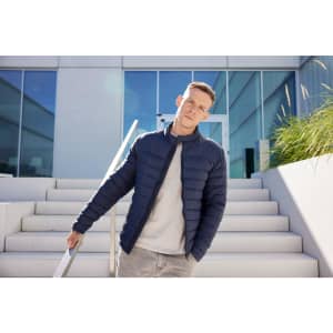 A navy padded jacket worn by a man standing on outdoor steps with modern architecture in the background.