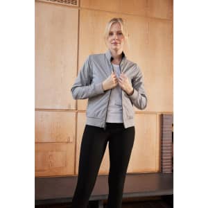 A light grey ladies blouson jacket is worn by a model, paired with black leggings against a wooden backdrop.