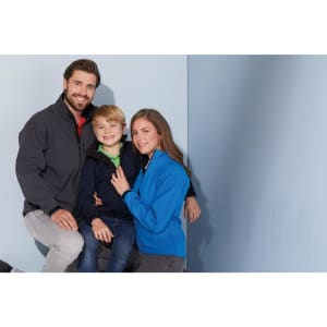 A family wearing softshell jackets in grey, navy, and blue against a light blue background. Each jacket has a logo.