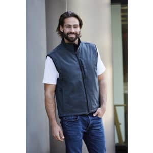 A men's softshell vest in dark grey, featuring a front zip and a logo. Worn over a white t-shirt and blue jeans.