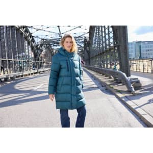 A teal ladies' winter long coat with a hood, featuring a puffer style, worn by a woman on a bridge.