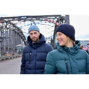 A man in a navy puffer jacket and a woman in a teal puffer jacket, both wearing beanies, stand outdoors.