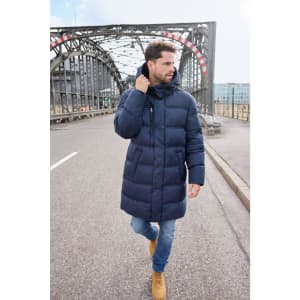 A man walks on a bridge wearing a navy long puffer coat, paired with jeans and tan boots.