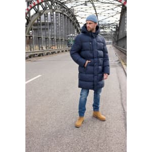 A man wearing a navy puffer coat stands on an empty road, paired with blue jeans and tan boots.