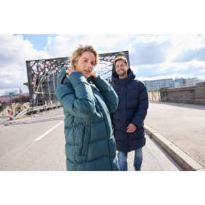 A puffer jacket in dark blue and a long coat in teal, both worn by people on a city street.