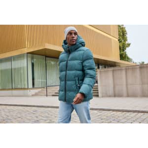 A puffer jacket in teal with a hood, worn by a person outdoors near a modern building.