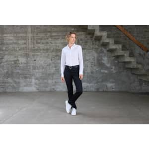 A white ladies shirt worn with black jeans and white sneakers, set against a concrete background with stairs.