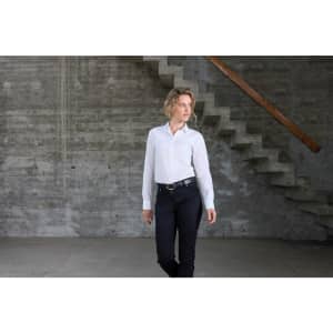 A white ladies shirt with long sleeves displayed on a model in a modern indoor setting, wearing black trousers.