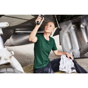A green work t-shirt worn by a woman, seated on a mat near an aircraft's undercarriage, holding a tool.