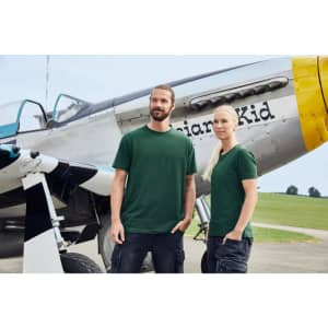 Two individuals wearing green BIO Stretch-T work t-shirts stand beside a vintage aircraft on a grassy field.