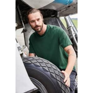 A man wearing a green BIO Stretch-T shirt adjusts a tyre near an aircraft. The shirt features a logo.
