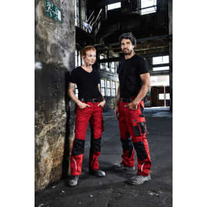 A pair of individuals in black t-shirts and red work trousers with black accents, standing in an industrial setting.