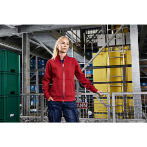 A red doubleface jacket with a zip, displayed on a model in a warehouse setting with storage units in the background.