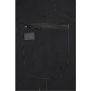 A close-up of black workwear pants featuring a zip pocket and contrasting stitching, with a logo on the pocket.