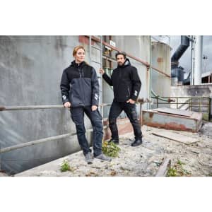 A padded hardshell workwear jacket in black and grey worn by two individuals posing against an industrial backdrop.