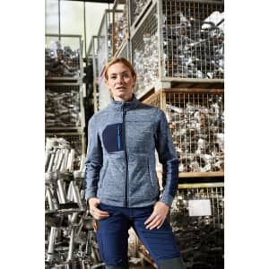 A women's polar fleece jacket in blue with a zippered front and a pocket, modelled against a backdrop of metal materials.