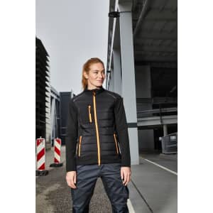 A black hybrid jacket featuring orange accents, with zippered pockets, set against an industrial background.
