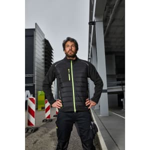 A hybrid jacket in black with neon green accents, featuring a zip front and a logo, worn by a model outdoors.