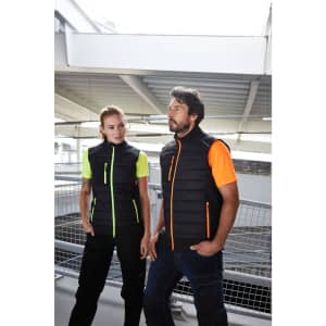 A black vest with neon orange and green accents, worn by two people in a modern indoor setting.