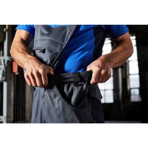 Workwear pants with bib in dark grey, featuring pockets and adjustable straps, being worn by a person.