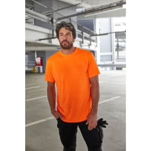 An orange work T-shirt is worn by a man standing inside a parking garage. The shirt has a logo on it.