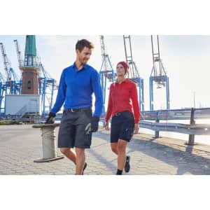 A blue long-sleeve polo shirt and a red polo shirt are worn by two models in a dockyard setting. Both have logos.