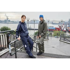 A navy blue and olive green rain jacket worn by two models, standing near a waterfront with ships in the background.