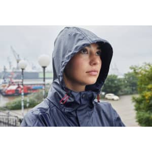 A rain jacket in navy blue worn by a person with a hood, set against a waterfront background.