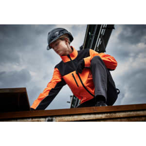A work jacket in orange and black, featuring a zip and pockets, worn by a person on a construction site.