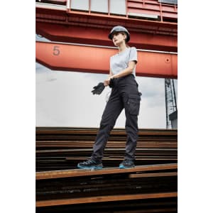 Workwear-Pants light in black, worn by a model in a construction setting, featuring side pockets and a logo.