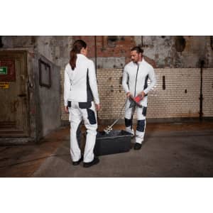 A pair of individuals wearing white and navy stretchfleece jackets in a gritty industrial setting.