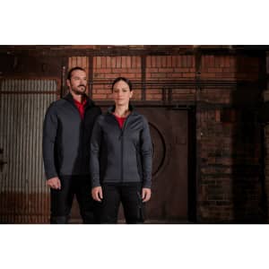 A grey ladies stretch fleece jacket is worn by a woman alongside a man in matching outerwear. Both stand against a rustic backdrop.