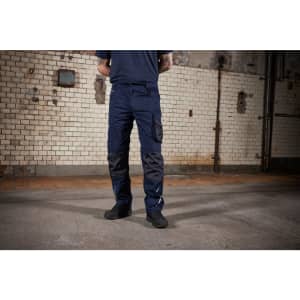 Navy work pants with multiple pockets and reinforced knee patches, set against a brick wall background.