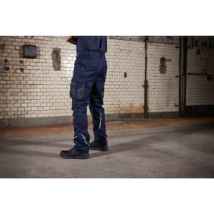 Navy blue work pants with multiple pockets, featuring reflective stripes, displayed in an industrial setting.