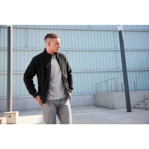 A polar fleece jacket in black, worn by a man, paired with a grey top and light jeans, set against a modern backdrop.