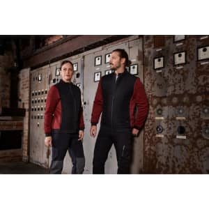 A pair of models wear a ladies padded hybrid jacket in black and red against an industrial backdrop. The jacket features branding.