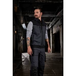 A man wearing a black and grey hybrid workwear vest in an industrial setting, showcasing a sleek design.