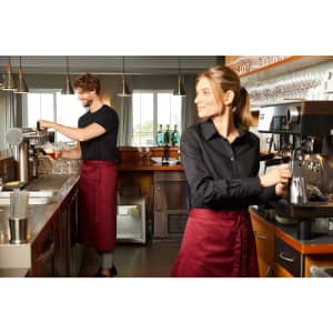 A maroon apron worn by a barista in a café setting, featuring two staff members at a coffee machine.
