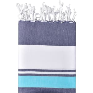 A striped beach blanket in navy blue, white, and turquoise, featuring decorative fringes along the edge and a logo.