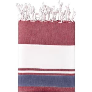 A striped beach blanket in burgundy, white, and navy, featuring fringed edges and a logo.