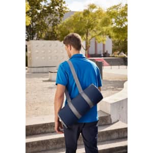 A picnic blanket in a navy blue carry bag is slung over the shoulder of a person wearing a blue shirt.