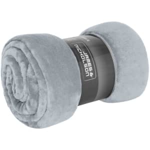 A rolled microfibre fleece blanket in soft grey, featuring a branded packaging label.